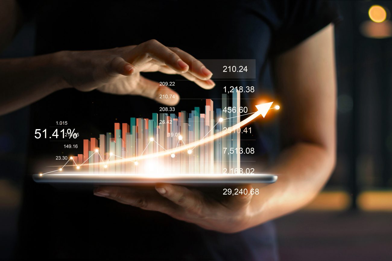businessman holding tablet and showing a growing virtual hologram of statistics, graph and chart with arrow up on dark background. Stock market. Business growth, planing and strategy concept.